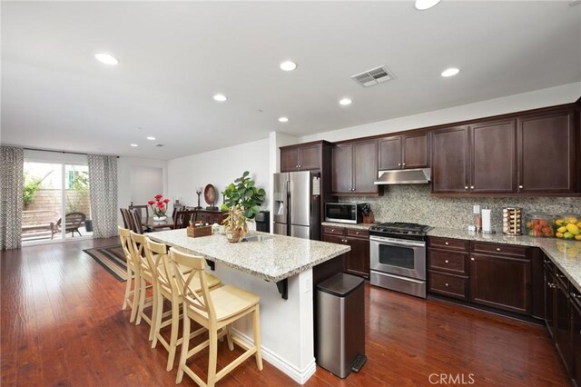 kitchen featuring visible vents, appliances with stainless steel finishes, a center island, light stone counters, and under cabinet range hood