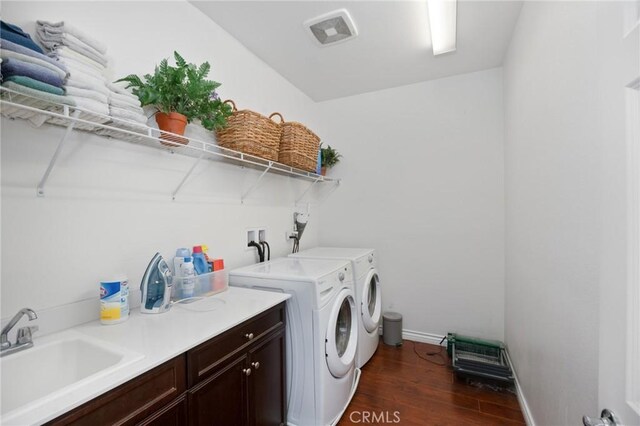 laundry room with cabinet space, a sink, baseboards, dark wood-style floors, and washer and clothes dryer