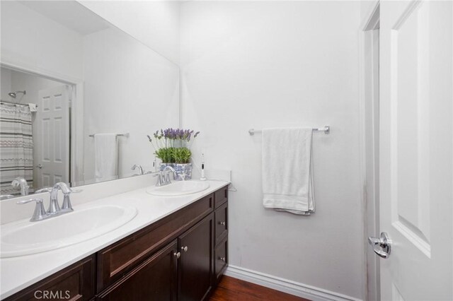 bathroom with double vanity, baseboards, a sink, and wood finished floors
