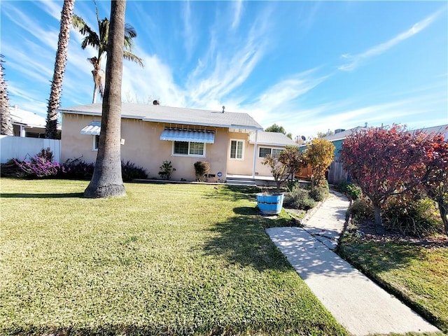 rear view of house with a lawn, fence, and stucco siding