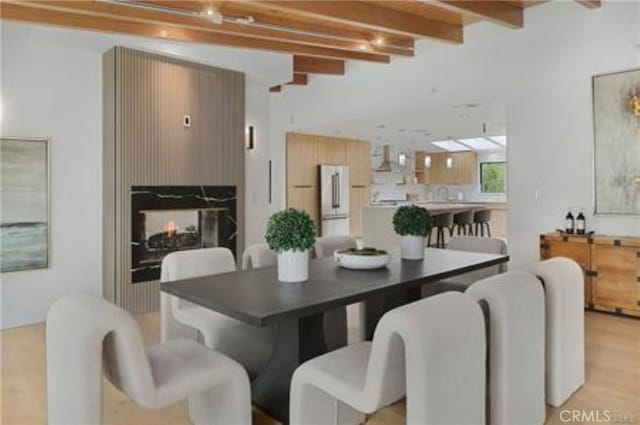 dining area with light wood-style floors, a multi sided fireplace, and beam ceiling