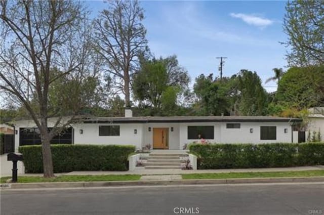ranch-style home featuring a chimney and stucco siding