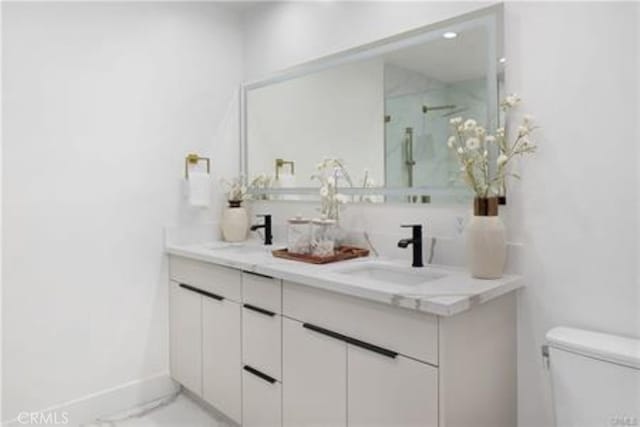 bathroom with double vanity, toilet, baseboards, and a sink
