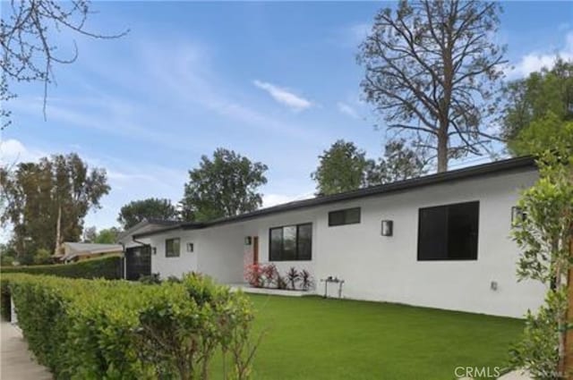 rear view of property featuring a lawn and stucco siding