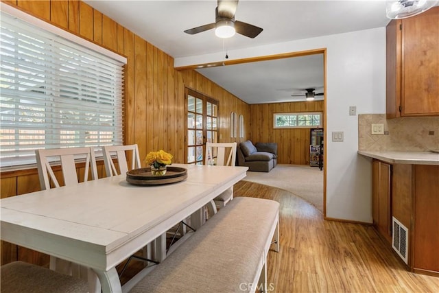 dining room featuring light wood-type flooring, a ceiling fan, wood walls, and visible vents