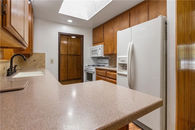 kitchen with a sink, a skylight, brown cabinetry, and white appliances