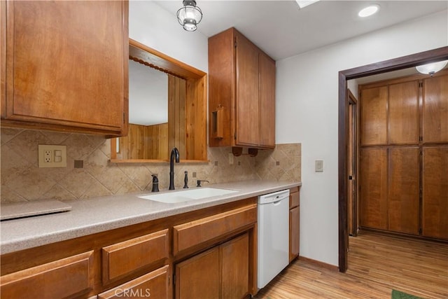 kitchen with white dishwasher, light countertops, a sink, light wood-style flooring, and backsplash