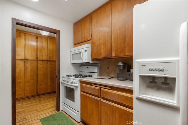 kitchen featuring brown cabinets, tasteful backsplash, white appliances, light countertops, and light wood-type flooring