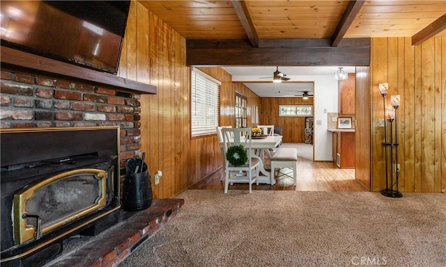 interior space with ceiling fan, a wood stove, wood walls, wooden ceiling, and beamed ceiling