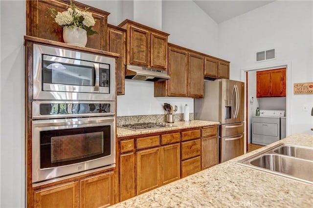 kitchen featuring brown cabinets, appliances with stainless steel finishes, under cabinet range hood, visible vents, and washing machine and dryer
