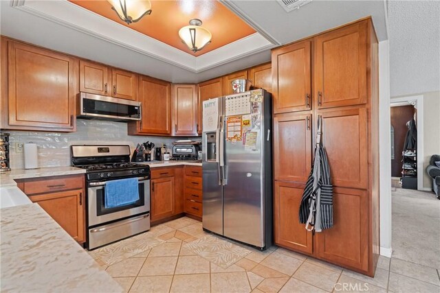 kitchen featuring stainless steel appliances, brown cabinetry, light tile patterned floors, and a raised ceiling