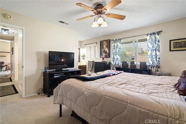 bedroom with ceiling fan, light carpet, a textured ceiling, and visible vents