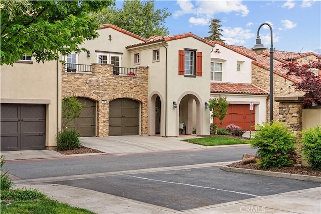 mediterranean / spanish-style house with an attached garage, a tile roof, stone siding, stucco siding, and a balcony