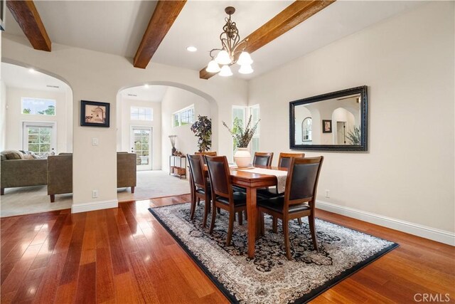 dining room featuring a healthy amount of sunlight, arched walkways, baseboards, and hardwood / wood-style flooring
