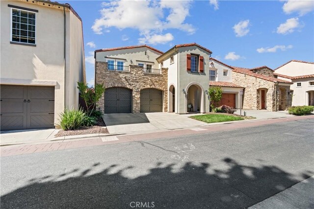 mediterranean / spanish-style home with an attached garage, stucco siding, concrete driveway, and stone siding