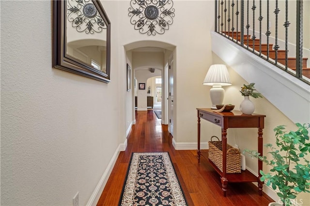 hallway with wood-type flooring, arched walkways, baseboards, and stairs