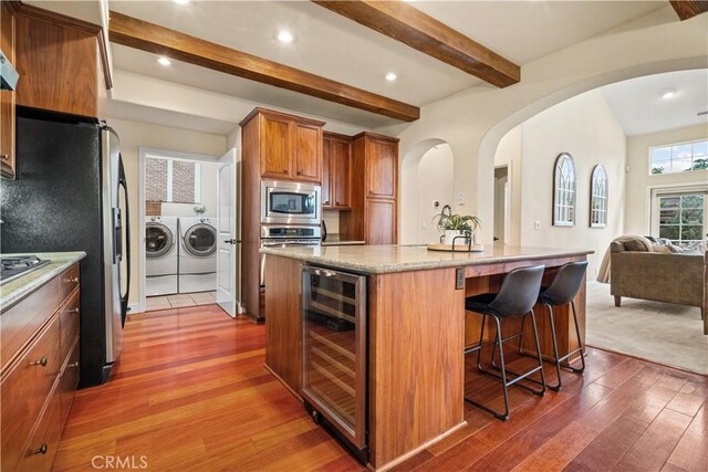 kitchen with wine cooler, wood finished floors, washing machine and dryer, arched walkways, and stainless steel appliances