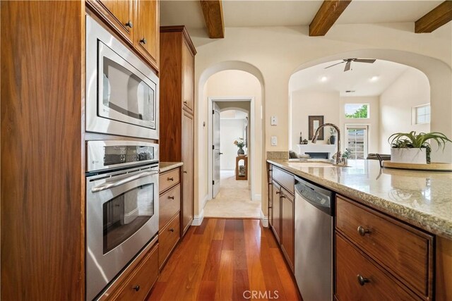 kitchen featuring dark wood-style flooring, a sink, arched walkways, brown cabinetry, and stainless steel appliances