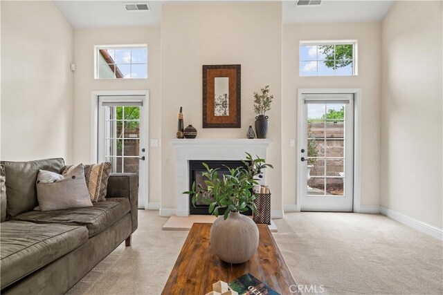 carpeted living room with baseboards, a high ceiling, and visible vents