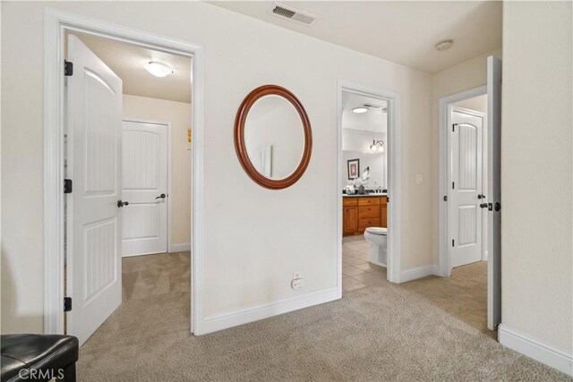 corridor featuring visible vents, baseboards, and light colored carpet