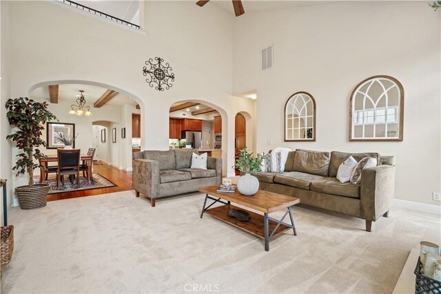 living area with high vaulted ceiling, beamed ceiling, a ceiling fan, and light carpet