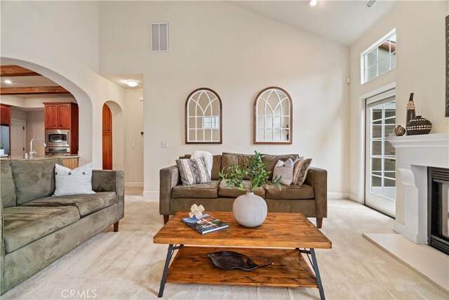 living area with high vaulted ceiling, light colored carpet, arched walkways, and visible vents