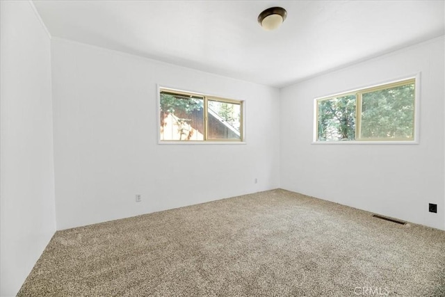 carpeted empty room featuring visible vents and a healthy amount of sunlight
