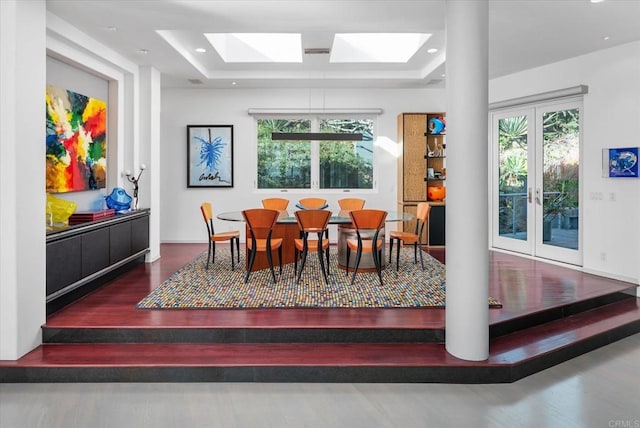 dining area with a skylight, a raised ceiling, french doors, and wood finished floors
