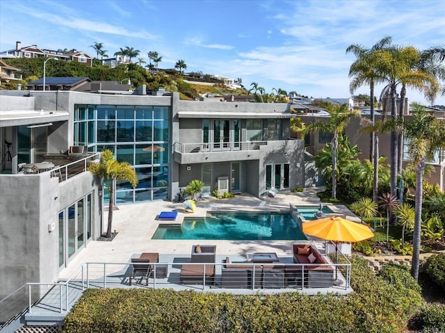 rear view of property featuring a patio, a balcony, and an outdoor pool