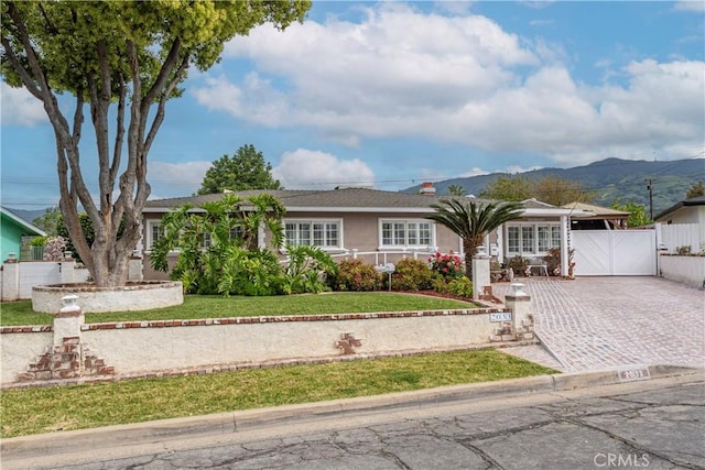 single story home featuring a front yard, a gate, fence, a mountain view, and stucco siding