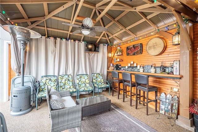 interior space featuring a bar, a ceiling fan, wooden walls, and carpet flooring