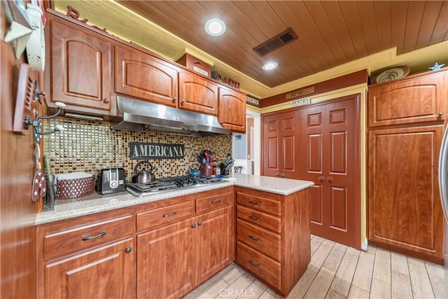 kitchen with wood ceiling, brown cabinetry, visible vents, stainless steel gas cooktop, and under cabinet range hood