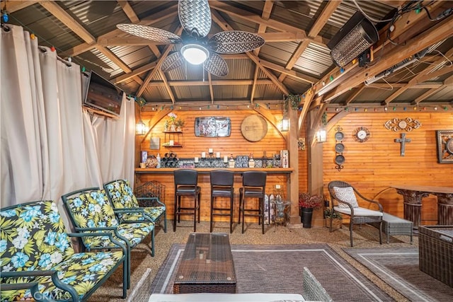 bar with wooden walls, carpet floors, a bar, and a ceiling fan