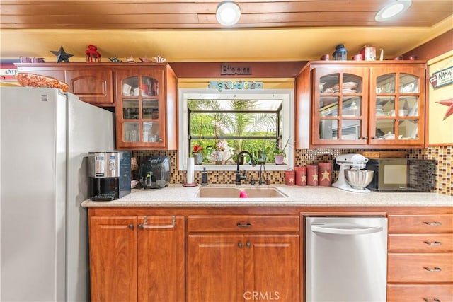 kitchen featuring stainless steel dishwasher, freestanding refrigerator, glass insert cabinets, light countertops, and a sink