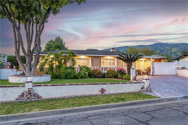 ranch-style house with fence, a gate, a lawn, a mountain view, and driveway
