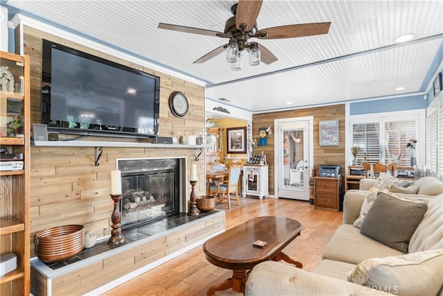 living room with wooden walls, a fireplace, a ceiling fan, and wood finished floors
