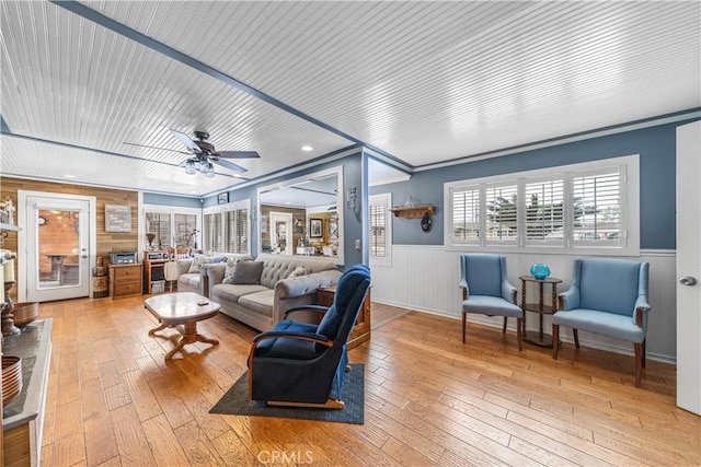 living room with crown molding, ceiling fan, wainscoting, and light wood-type flooring