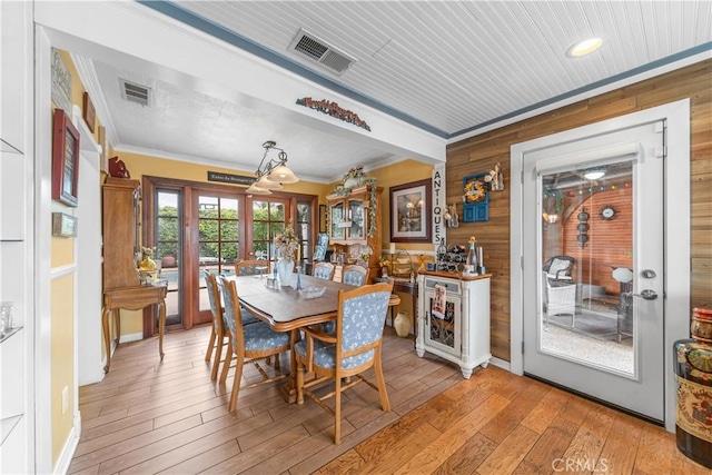 dining room with crown molding, wood walls, and visible vents