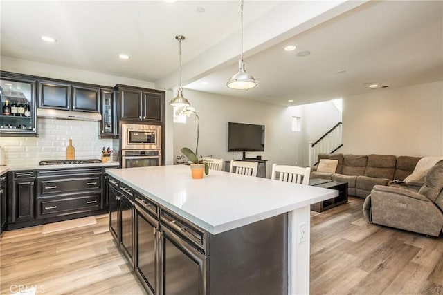 kitchen featuring light countertops, backsplash, stainless steel appliances, and light wood finished floors