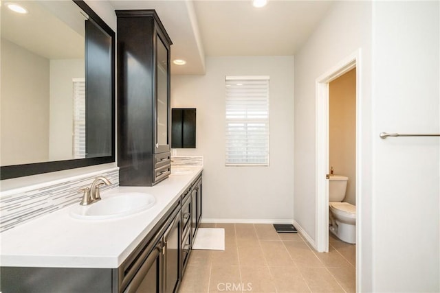 bathroom featuring double vanity, toilet, baseboards, recessed lighting, and a sink