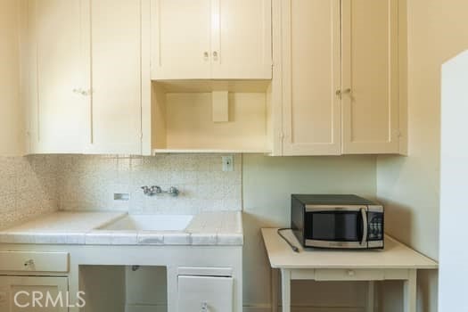 432 N Virgil Ave, Los Angeles, CA 90004 - kitchen featuring decorative backsplash, light countertops, white cabinetry, stainless steel microwave, and a sink