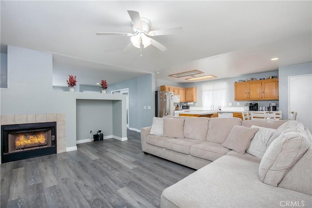 living area featuring a ceiling fan, recessed lighting, baseboards, a tiled fireplace, and wood finished floors