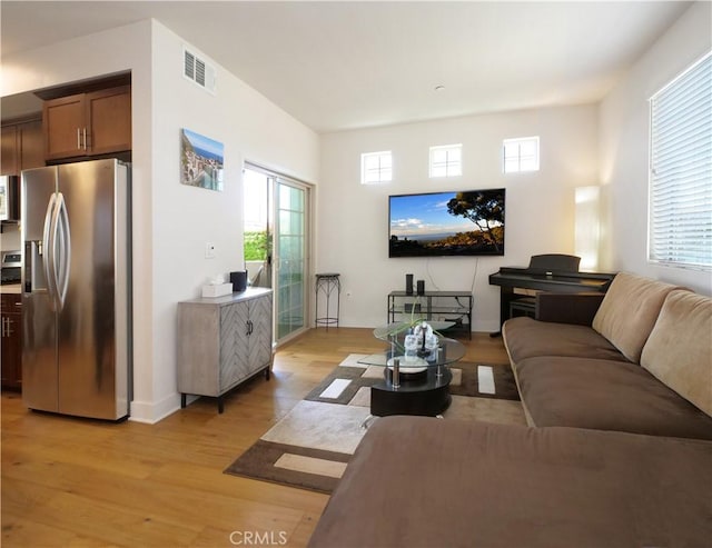 living room featuring visible vents, light wood-style flooring, plenty of natural light, and baseboards