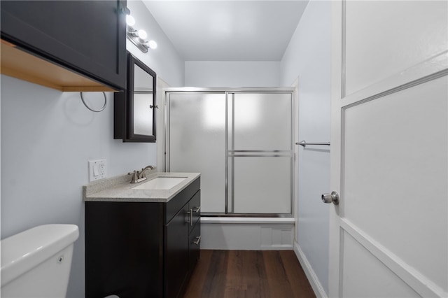 bathroom featuring toilet, enclosed tub / shower combo, wood finished floors, and vanity