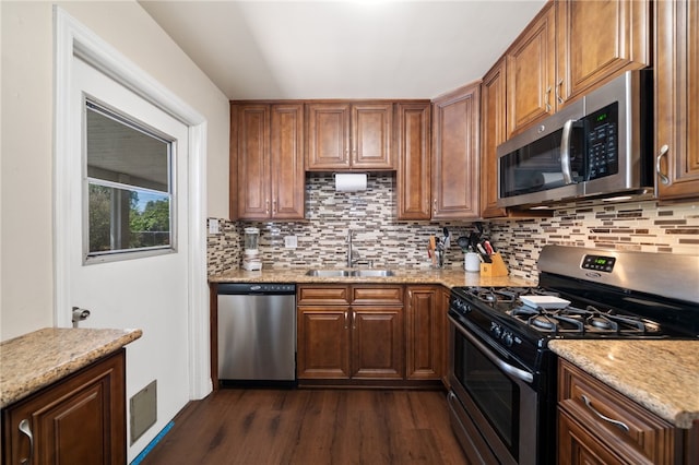 kitchen featuring dark wood-style flooring, light stone counters, a sink, stainless steel appliances, and decorative backsplash