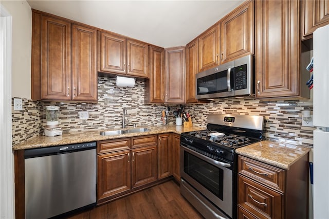 kitchen with brown cabinets, a sink, dark wood finished floors, stainless steel appliances, and decorative backsplash