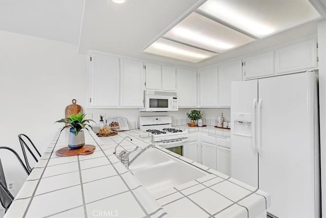 kitchen featuring a peninsula, white appliances, tile counters, white cabinetry, and a sink