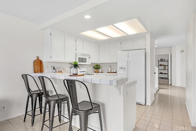 kitchen with tile countertops, a peninsula, light tile patterned floors, and white appliances