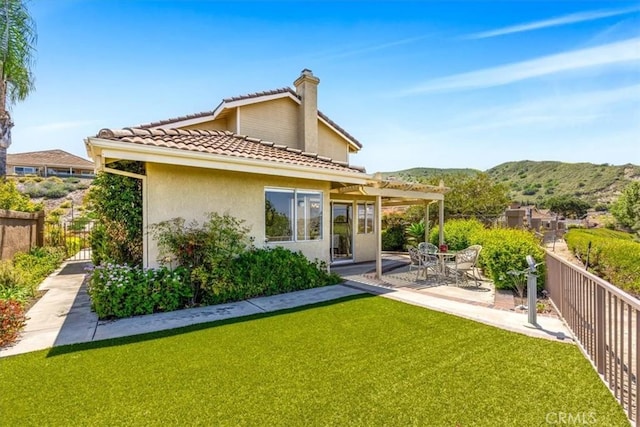 back of house with a fenced backyard, a mountain view, a chimney, a patio area, and a yard