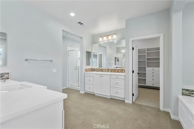 full bath featuring a walk in closet, a stall shower, two vanities, a sink, and baseboards